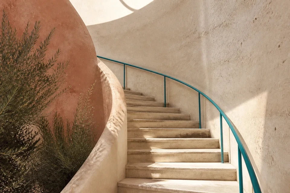 A curved stone staircase with a teal handrail in soft daylight